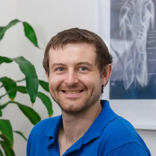 Daniel in a blue polo shirt smiling in front of a plant.